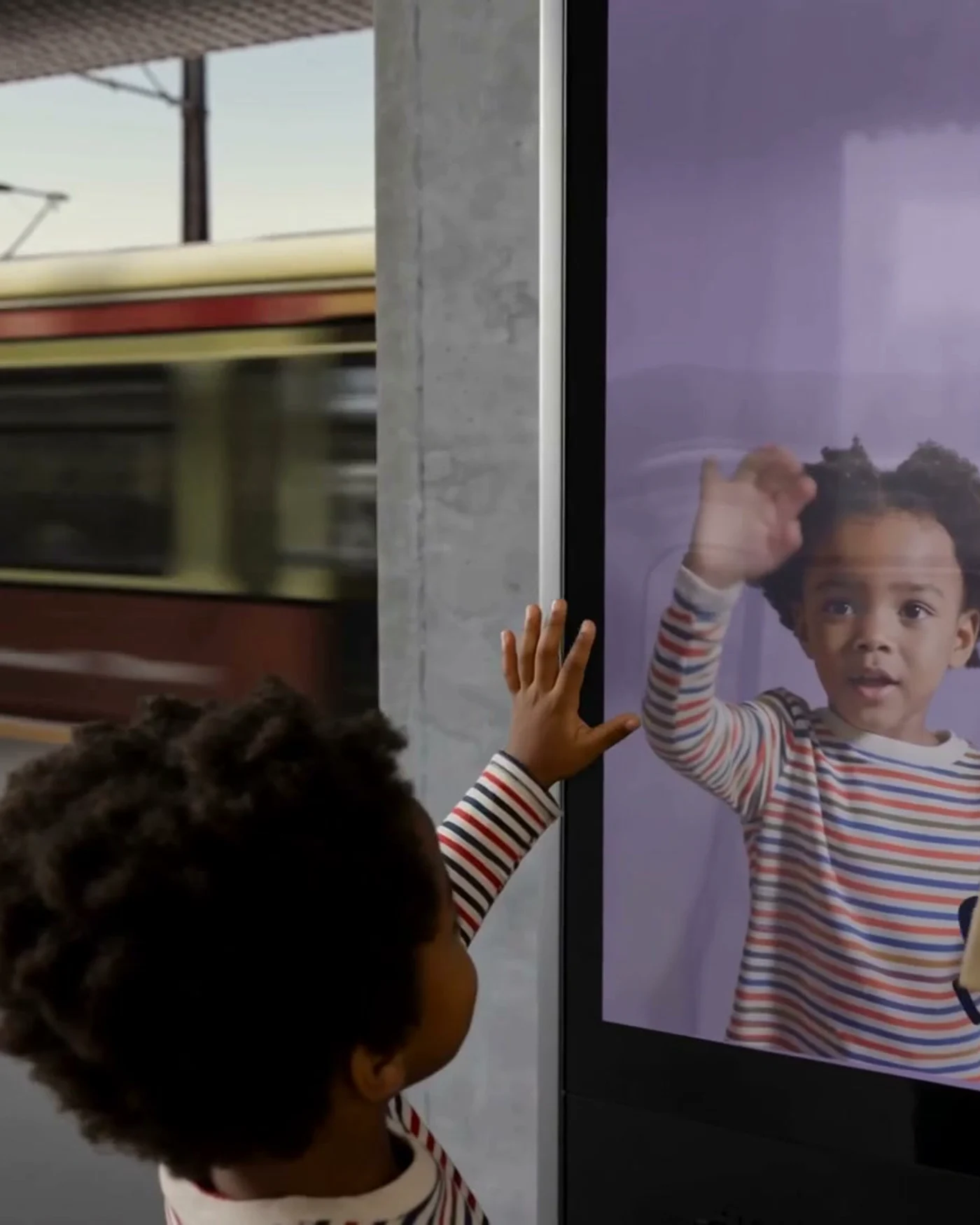 Child reaching toward the live Spot yourself? camera feed on the kiosk