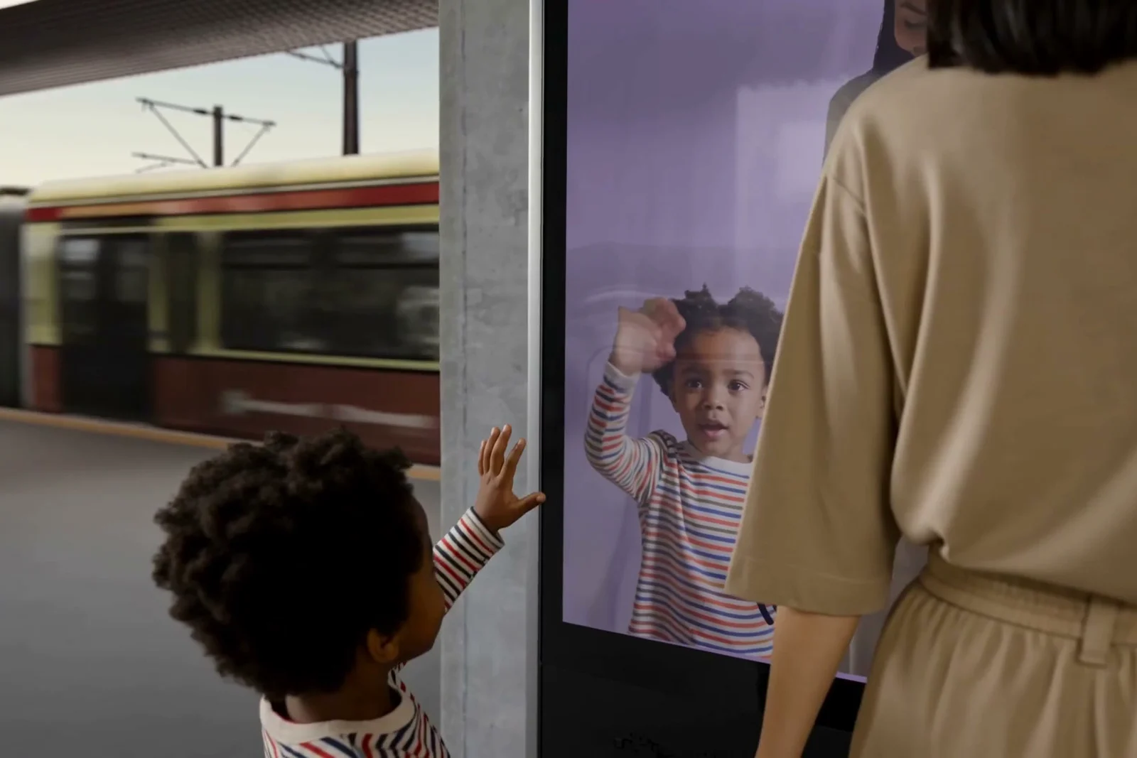 Mother and child watching the interactive screen while a train blurs past