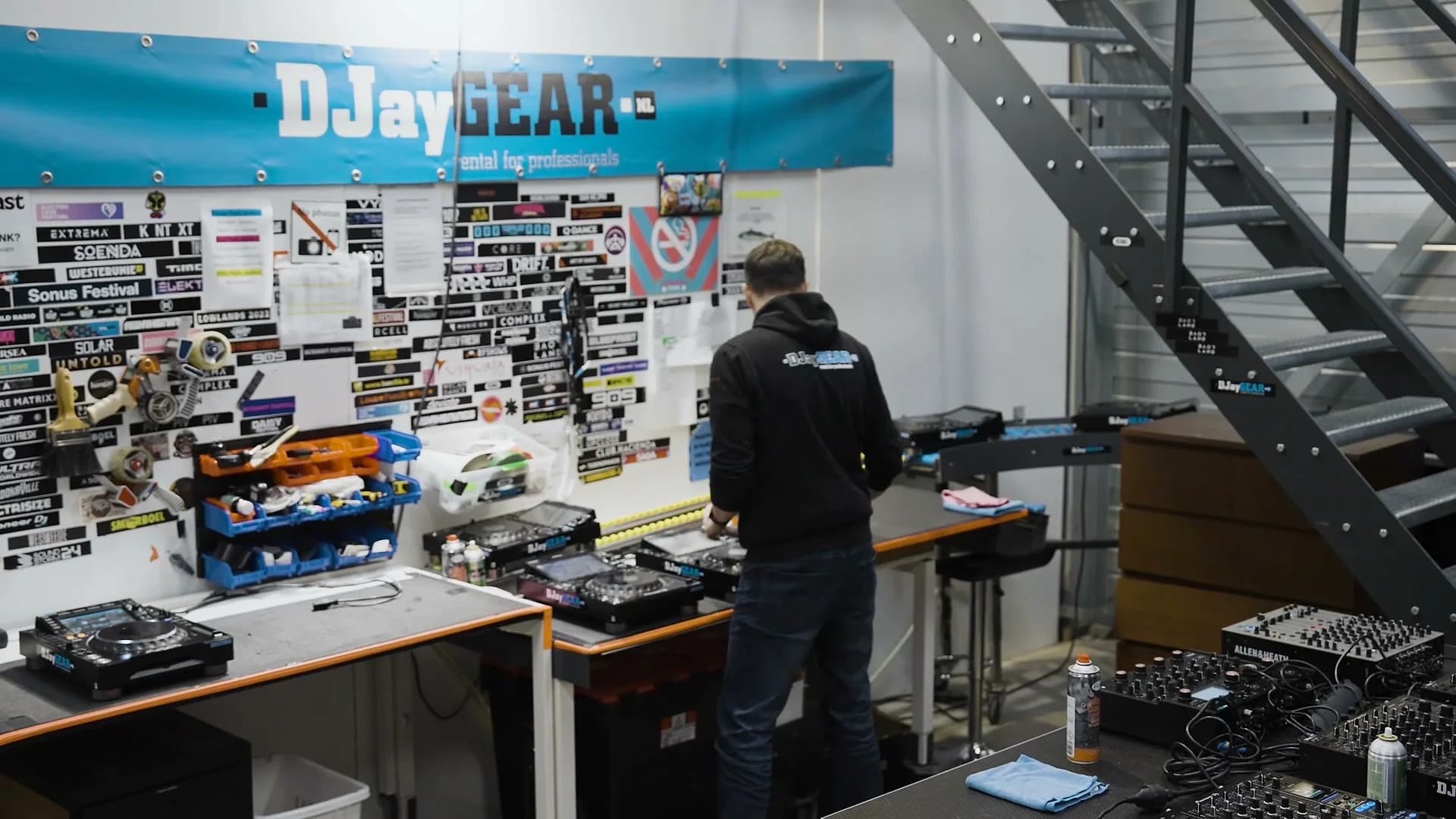 Technician in a DJayGear hoodie working CDJs at the branded workshop bench