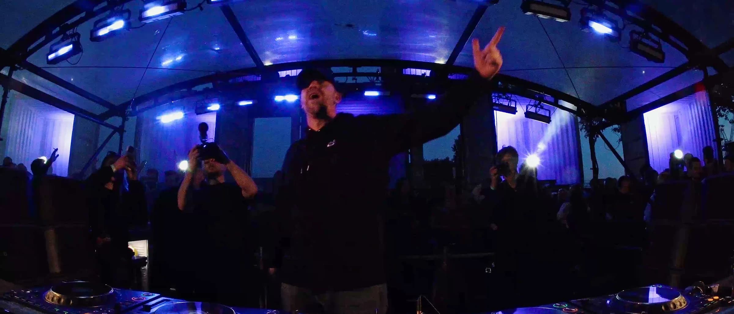 DJ pointing to the crowd behind a lit mixer under blue stage lights