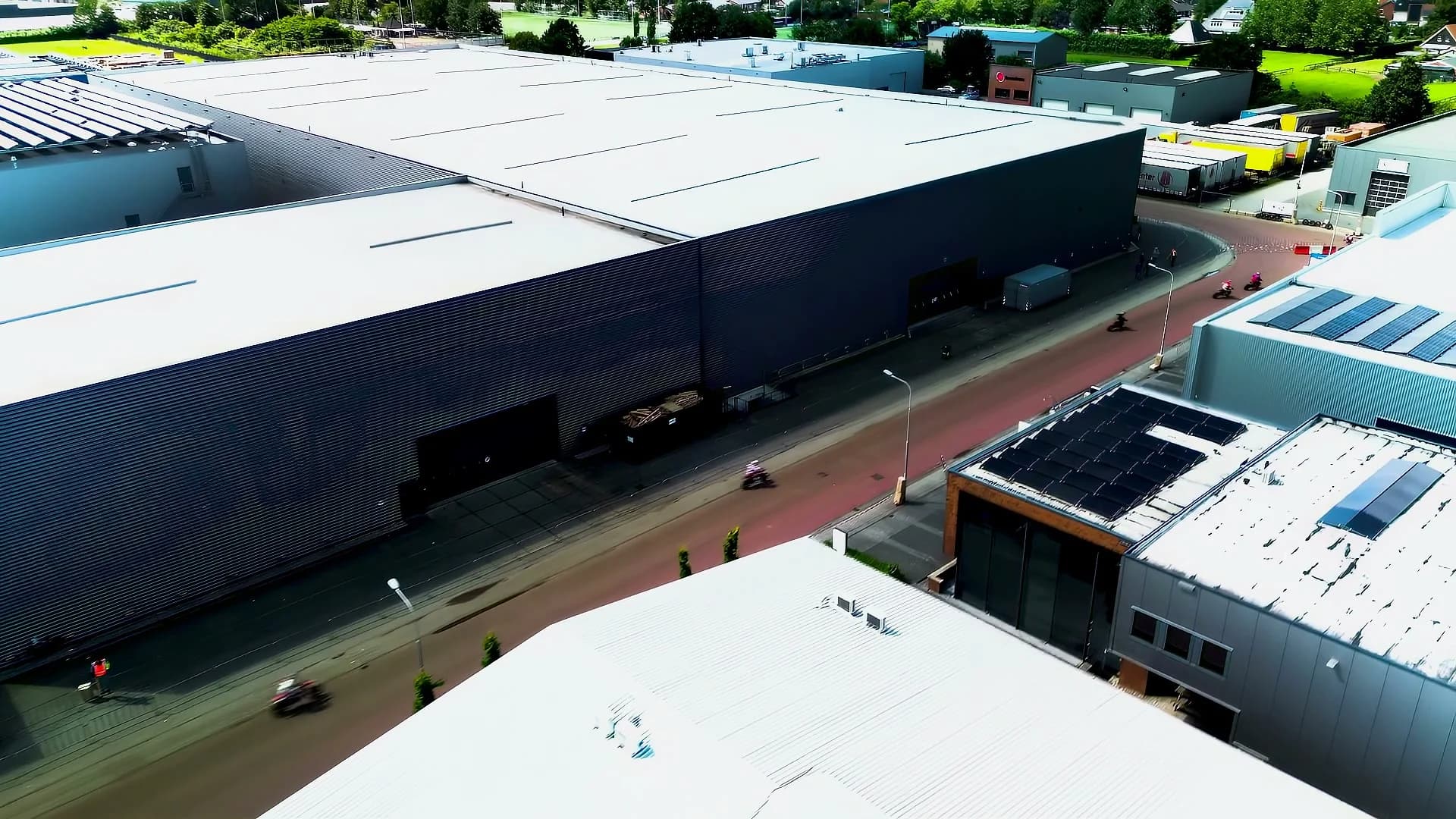 Drone view of a pink supermoto cutting past industrial warehouses